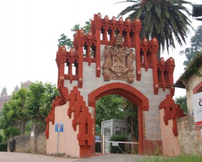 Das Tor der alten Universität von Comillas<br /><br />errichtet im Neugotischen-, Mudéjar- und Jugendstil, stammt aus dem  Jahr 1889 und ist der Eingang zum Anwesen von Cardosa, in dem sich das Seminar befindet. Es ist eine harmonische Mischung aus Ziegeln, glasierter Keramik mit metallischem Glanz und behauenen Steinen.<br />Auf dem von zwei Kindern in aufwändiger Kleidung getragenen Wappen, über dem sich eine Krone befindet, sieht man die päpstliche Tiara und den Papstschlüssel zusammen mit den Jesuiten-Monogramm IHS (Iesum Habemus Socium - „Wir haben Jesus als Gefährten“). Die Figuren der Kinder werden von zwei Neidköpfe (quimeras) mit orientalischem Einfluss getragen.