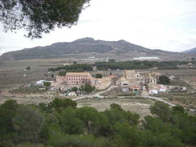 Die Colonia, betrachtet von oben (cerro de Santa Eulalia),von links nach rechts die wichtigsten Gebäude: <br />Die Getreidemühle, die Hauptstraße (calle Salinas), der Turm der Alkohol-Fabrik; gleich daneben die Kapelle und der Palast der Grafen. <br />Das Foto stammt von der Wikipedia-Seite über die Colonia de Santa Eulalia und ist bei Namensnennung des Autoren (Enrique Íñiguez Rodríguez [Qoan]) gemeinfrei