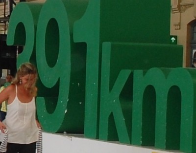 Wo befindet sich die junge Dame und was sagt die Kilometerangabe im Hintergrund aus?
